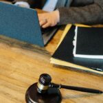 From above of crop anonymous male lawyer in formal clothes typing on laptop while sitting at wooden table with stack of documents and gavel